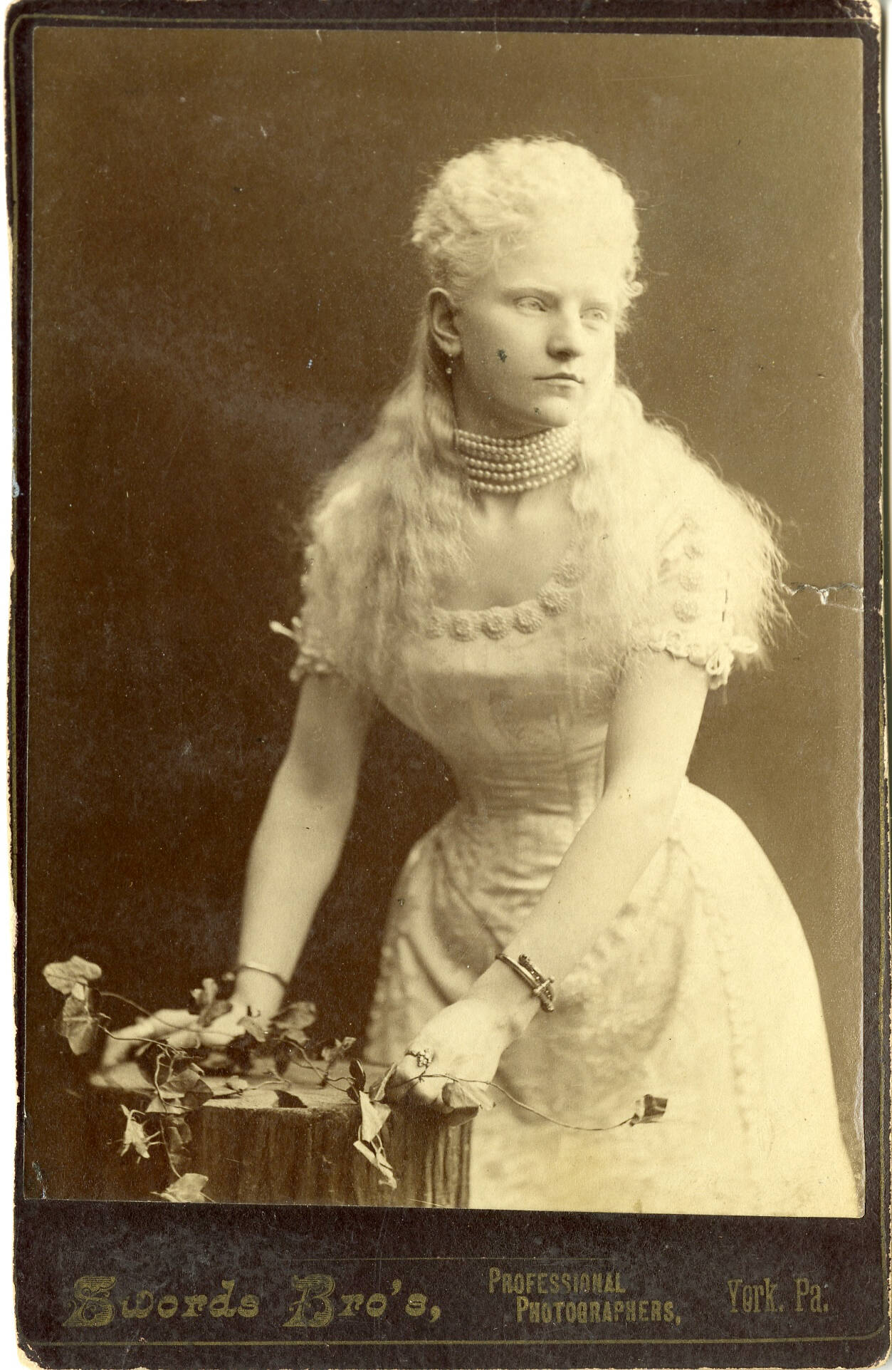 Portrait ofa. woman in a light colored dress, leaning against something. She appears to be an albino woman.